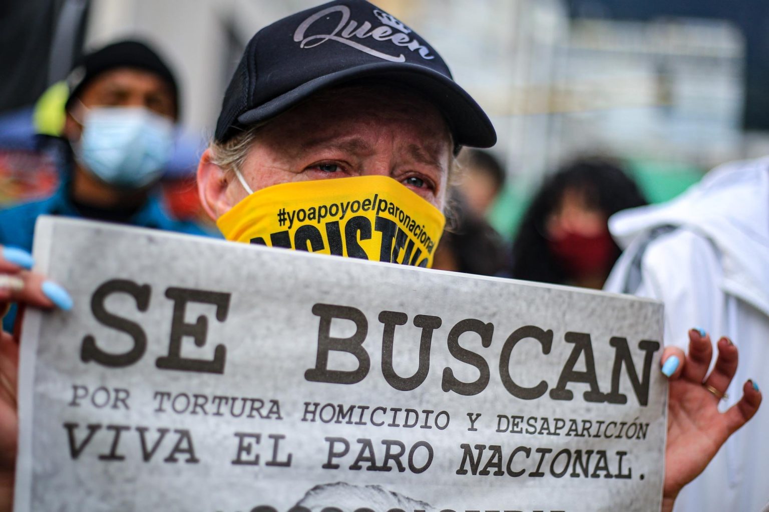 A protester cries while holding a sign during the social uprising in Bogotá, Colombia, June 2021. The sign reads: “Wanted for torture and disappearance. Long live the national strike.” Photo © Daniela Diaz.